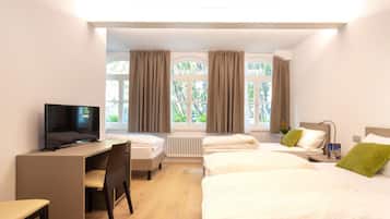 A hotel room with a desk, two beds, a TV, and large windows with curtains.