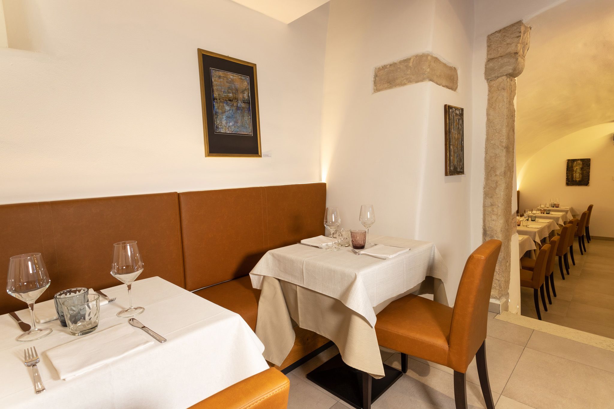 Comedor con mesas dispuestas para dos, con manteles blancos y asientos tipo banca acolchados en marrón.