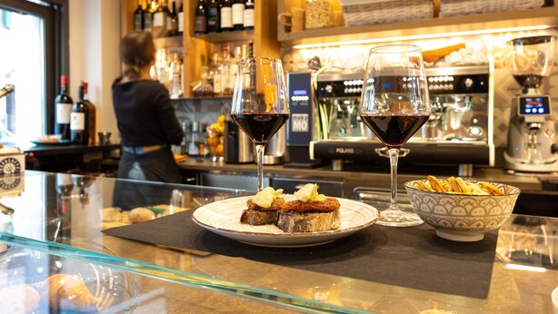 Una zona de bar con una vitrina, un plato de comida, dos copas de vino y un bol de aperitivos.