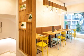 A modern cafe with wooden partitions, yellow and blue chairs, and a large window offering a view of the street. - Locanda Le Due Travi (Trento)