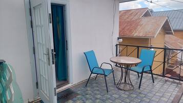 Un balcon avec une table et des chaises, une porte et une vue sur les bâtiments voisins.