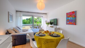 A modern room with a bed, a dining table with breakfast, a TV, and a colorful fish painting. - Large studio, feet in the water! (Bénodet)