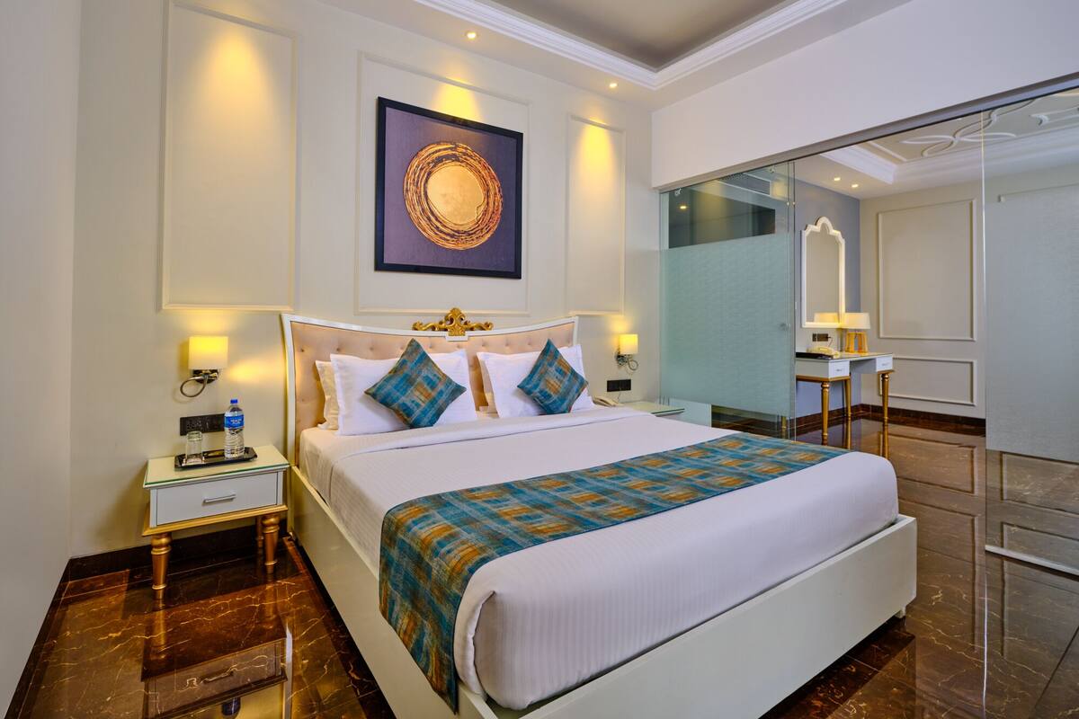 A hotel room with a large bed, a bedside table, a nightstand, a mirror, and a wall-mounted artwork.
