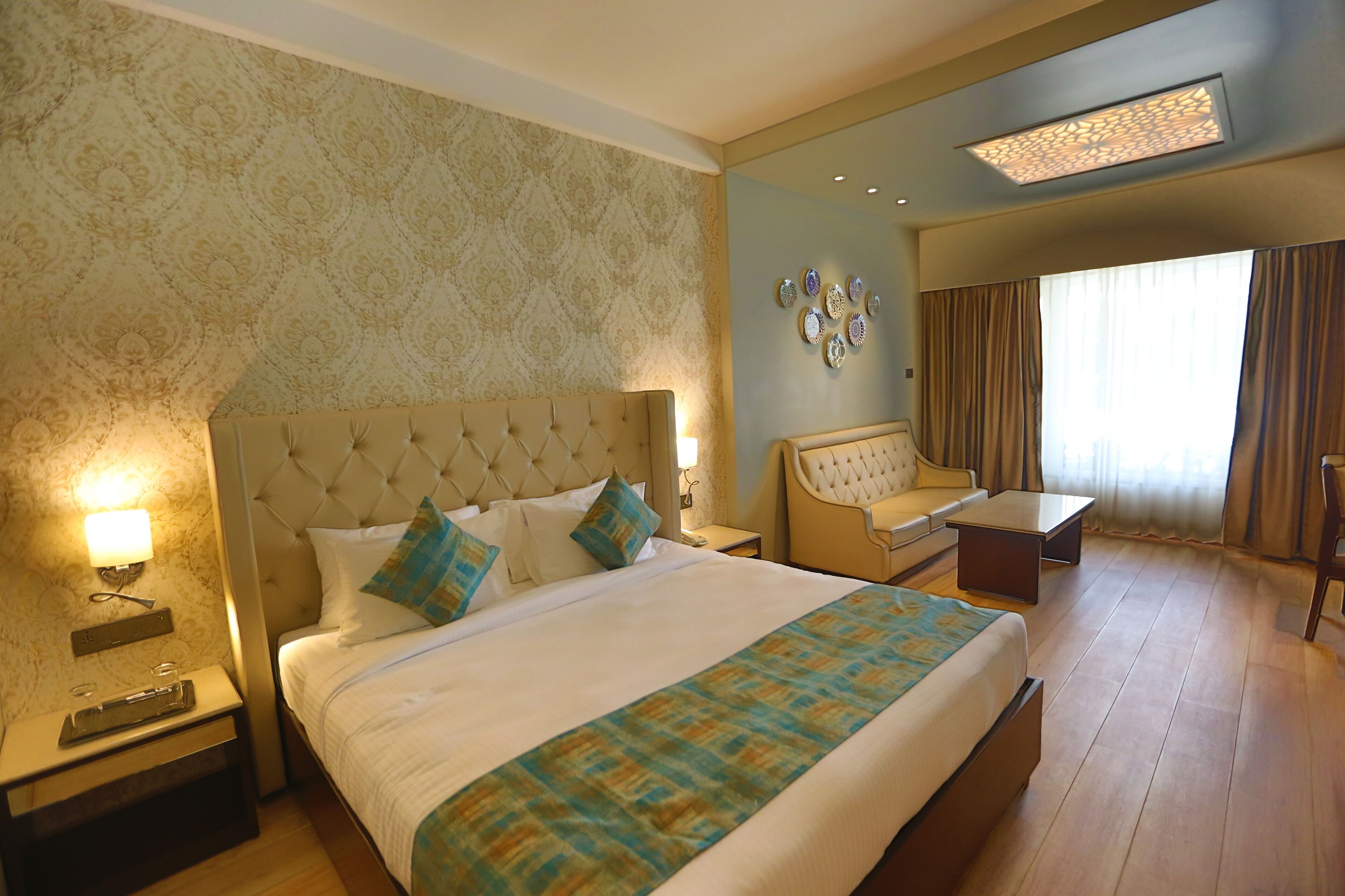 Habitación de hotel con una cama grande, una zona de estar con sofá y una mesa, y vistas al exterior a través de una ventana.