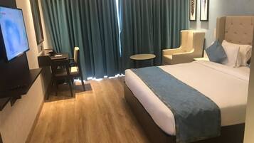 Una camera d'albergo con un letto, una scrivania, una sedia, un tavolino e una televisione.