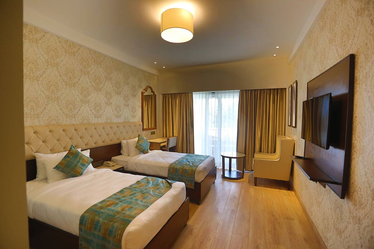 A hotel room with two beds, a TV, a small table, and a chair.