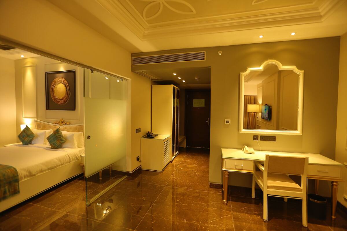 A hotel room with a bed, a desk, a chair, a mirror, and a wall-mounted artwork.