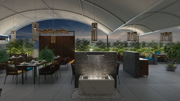 An outdoor dining area with tables and chairs, a stone wall with a water feature, hanging lanterns, and potted plants. - Enrise by Sayaji Rau (Indore)