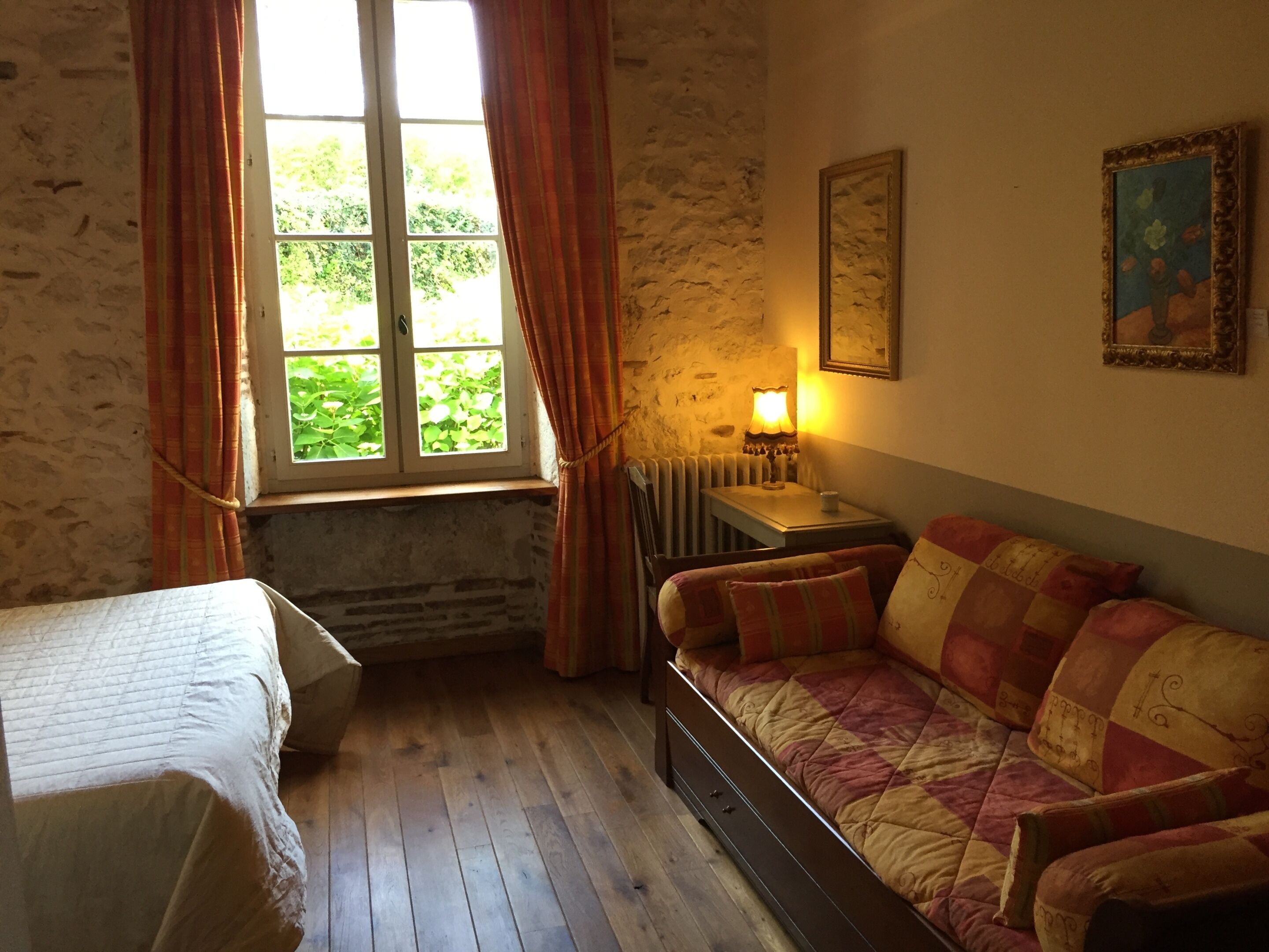 A room with a bed, a sofa, a window with curtains, a radiator, and a lamp.