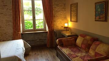 A room with a bed, a sofa, a window with curtains, a radiator, and a lamp.