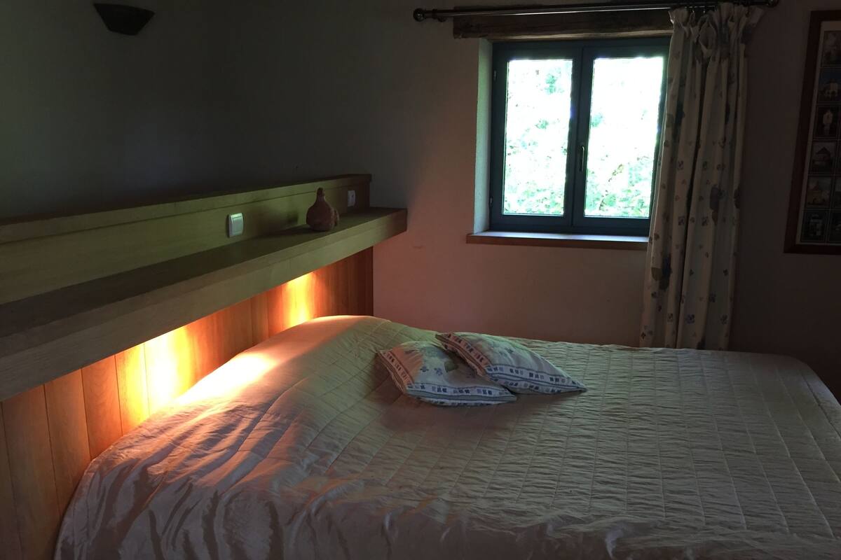 Ein Schlafzimmer mit Bett, Fenster mit Vorhängen und einem Regal mit Dekoration.