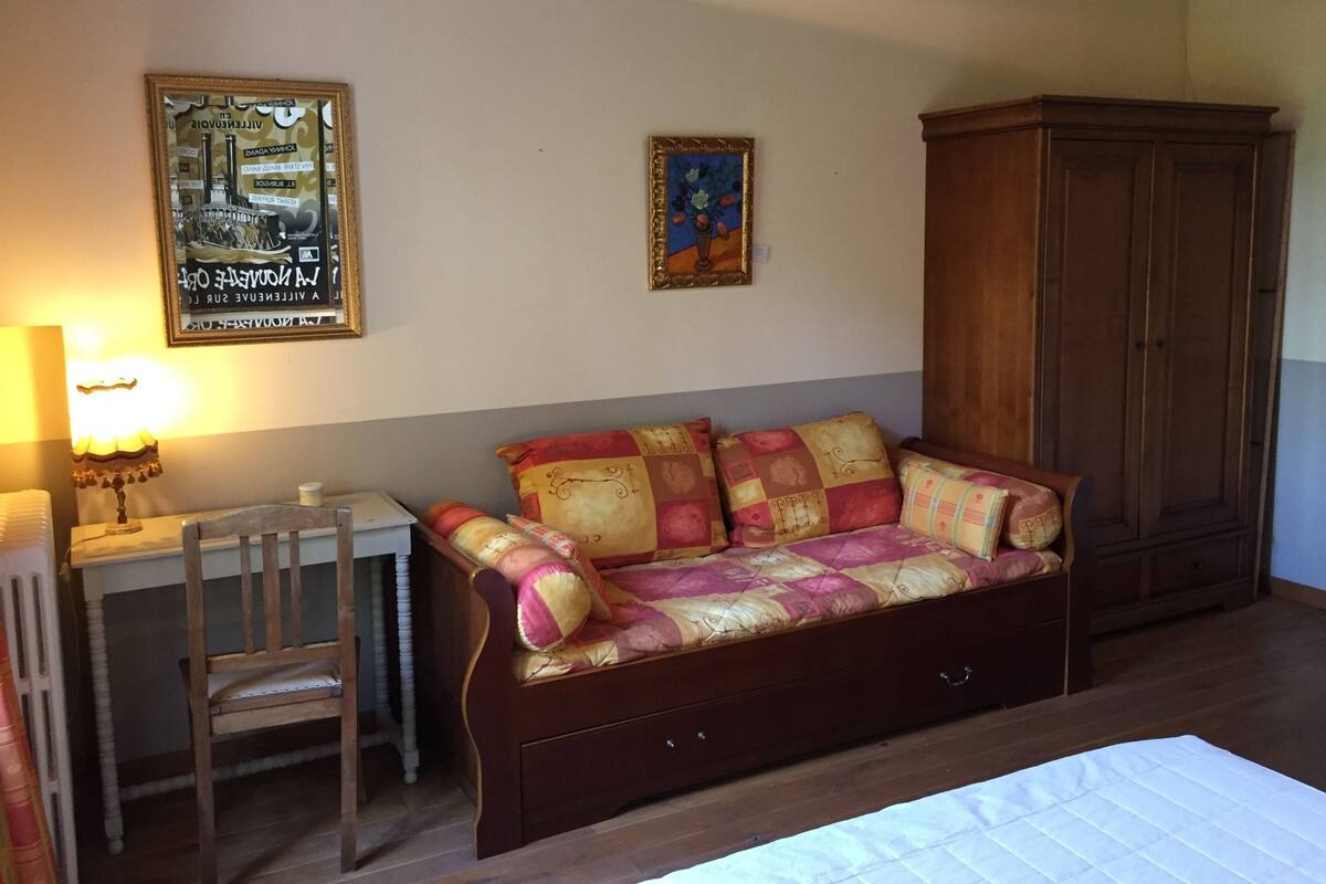 Ein Zimmer mit einer Holzcouch, einem Schreibtisch mit Lampe und einem Schrank.