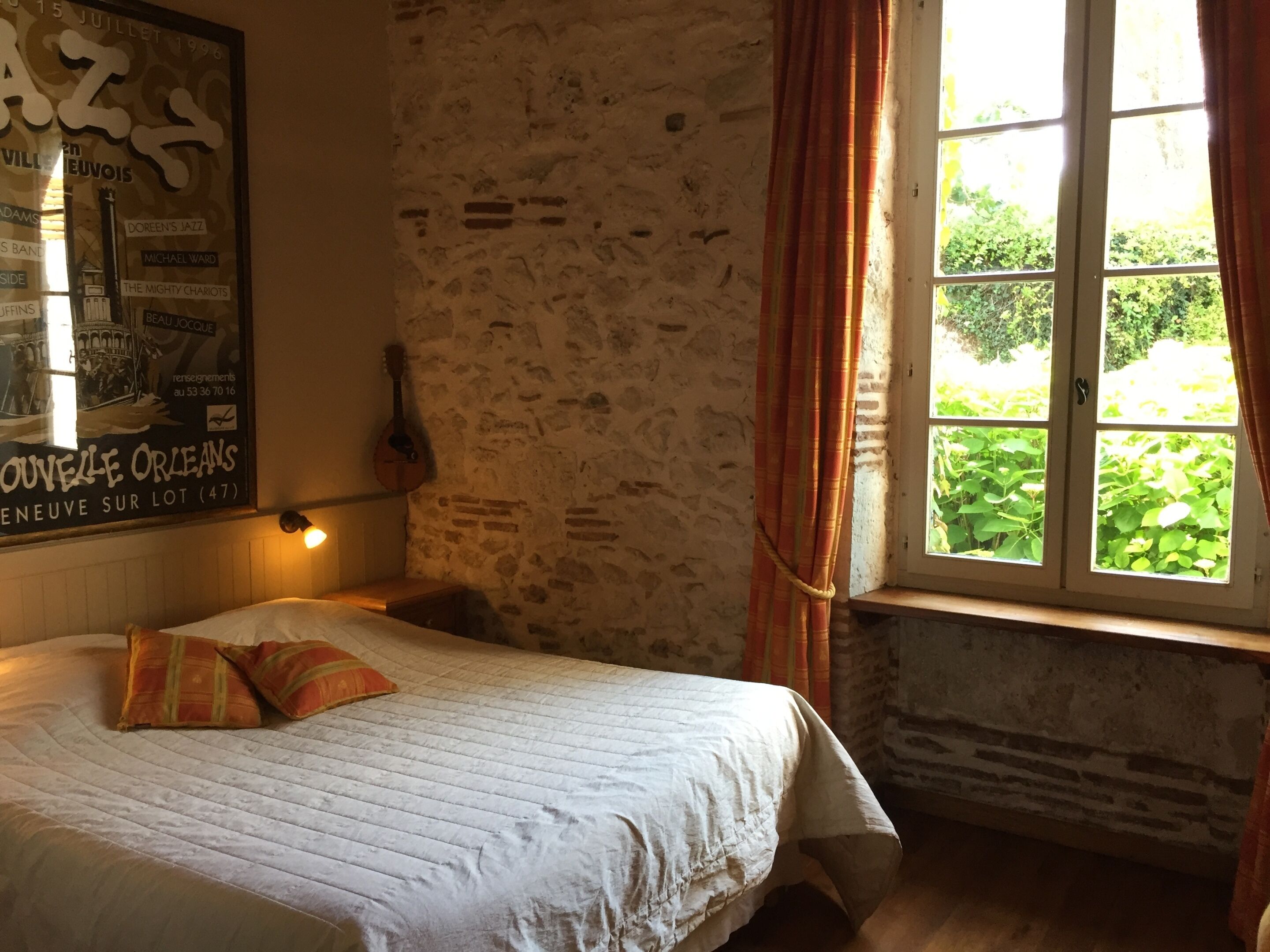 Un dormitorio con cama, guitarra, cartel y ventana con cortinas.