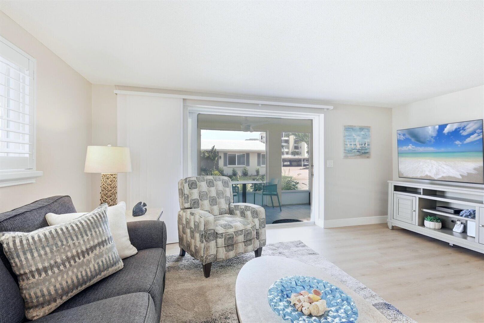 A living room with a sofa, armchair, coffee table, TV, and a view through a glass door to an outdoor patio.