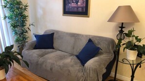 Ein graues Sofa mit zwei blauen Kissen, einem Holztisch, einer Stehlampe und Topfpflanzen.