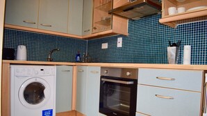 Eine kleine Küche mit Waschmaschine, Backofen und dunkelblauer Fliesenspiegel.