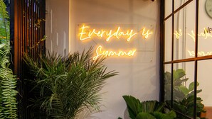 A cozy outdoor seating area with a neon sign, potted plants, and a white chair. - Tropical Summer Hostel (Bangkok)