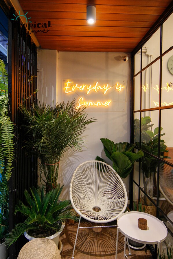 Uma área de estar acolhedora ao ar livre, com um letreiro de neon, plantas em vasos e uma cadeira branca.