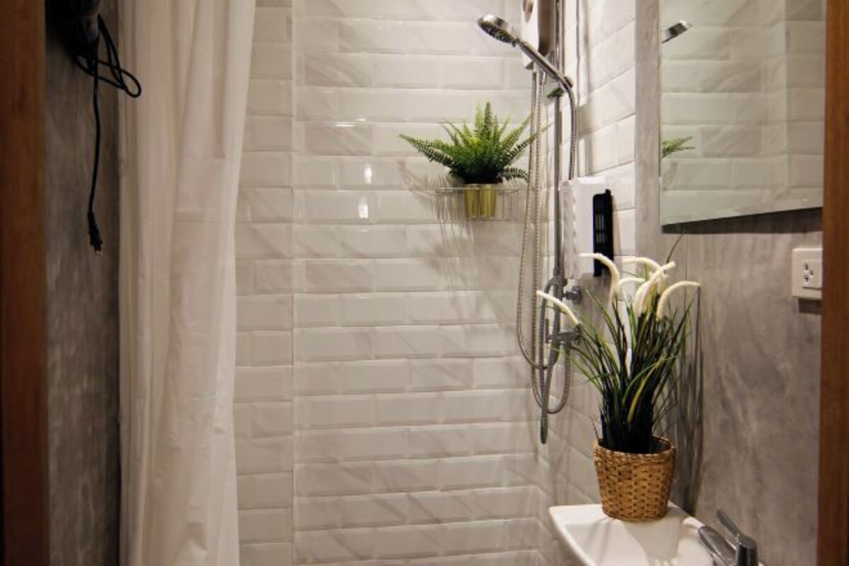 A modern bathroom with a shower, a sink, and a mirror. There are two potted plants on the wall.