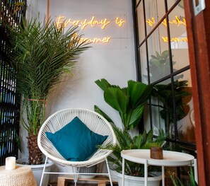 A wicker chair with a teal cushion, a small round table, and a large potted plant. - Tropical Summer Hostel (Bangkok)