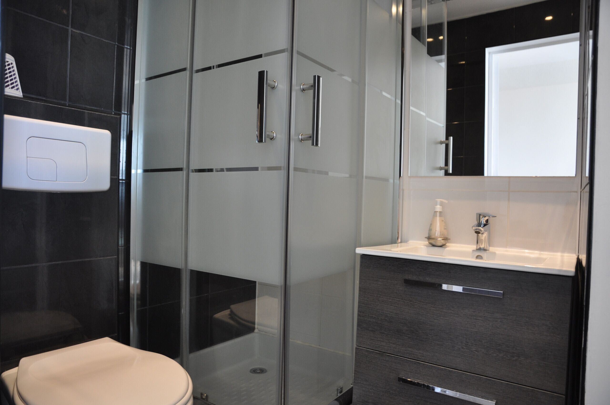 Une salle de bain moderne dotée d’une douche à parois de verre, de toilettes et d’un meuble-lavabo avec un miroir.