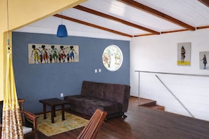 Ein Wohnzimmer mit blauer Wand, einem braunen Sofa, einem kleinen Tisch, einer blauen Pendelleuchte und Kunstwerken.