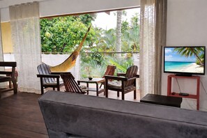 A living room with a sofa, two wooden chairs, a small table, a hammock, and a TV on a stand. - Apartment duplex T3 (90m²) hyper center (Praia de Pipa)