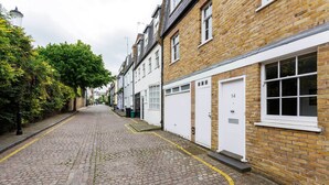 A cobblestone street lined with brick buildings, each with a white garage door and a number plaque. - Ladbroke Walk, by Veeve (London)