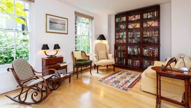 A cozy living room with a rocking chair, a sofa, a bookshelf, and a window with a view of greenery. - Ladbroke Walk, by Veeve (London)