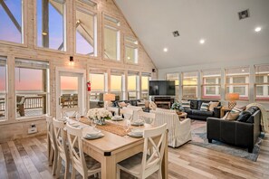 Un vaste espace de vie doté d’un haut plafond, de grandes fenêtres, d’une table à manger avec des chaises, et d’un coin salon avec des canapés et un téléviseur.