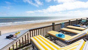 A wooden deck with striped lounge chairs and a wooden railing overlooking a beach. - Beachfront | Game Room, Hot Tub & Ocean Views (Bolivar Peninsula)