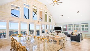 A spacious living area with a large kitchen island, wooden flooring, and large windows offering ocean views. - Beachfront | Game Room, Hot Tub & Ocean Views (Bolivar Peninsula)