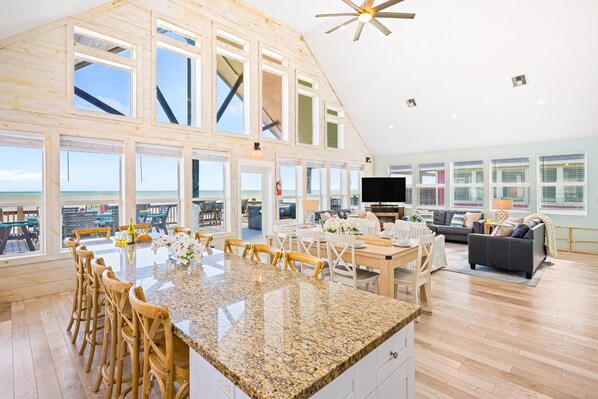 A spacious living area with a large kitchen island, wooden flooring, and large windows offering ocean views.