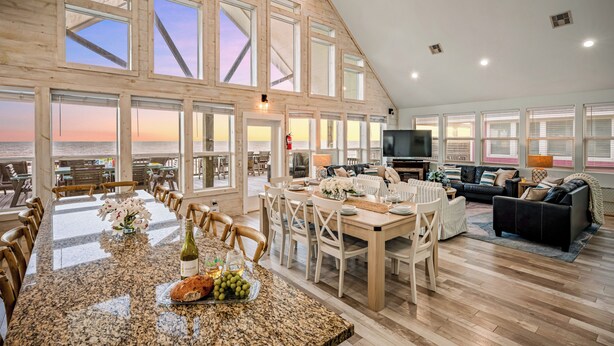 A spacious interior with a large dining area, a living room with a sofa and TV, and large windows offering a view of the ocean. - Beachfront | Game Room, Hot Tub & Ocean Views (Bolivar Peninsula)