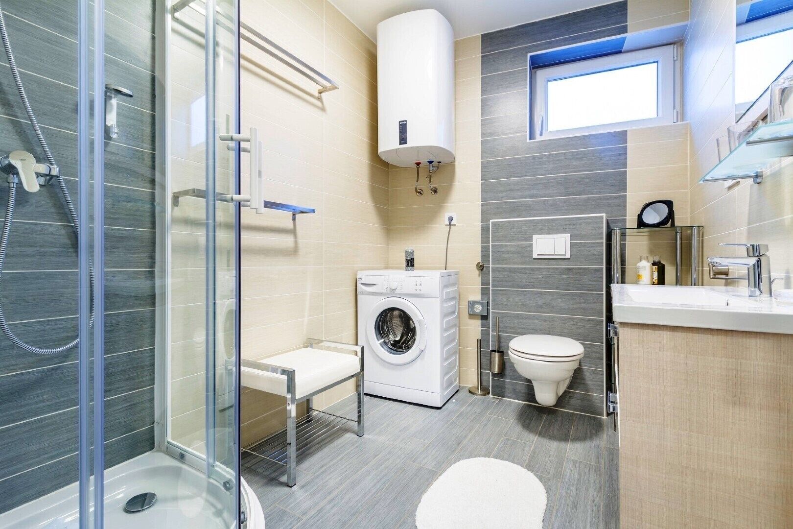 Un baño moderno con cabina de ducha de vidrio, lavadora integrada, inodoro y lavamanos con espejo.
