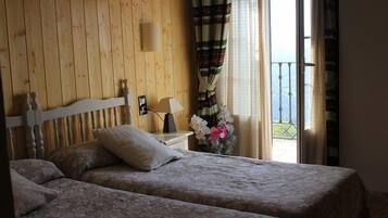 A room with two beds, a wooden headboard, a nightstand with a lamp, and a window with curtains.