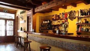 Een bar met houten krukken, een betegelde achterwand en gevulde flessenrekken.