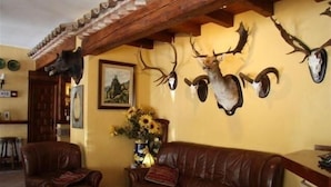 Een kamer met een bruine leren bank, een houten bijzettafeltje en een muur versierd met opgehangen dierenkoppen.