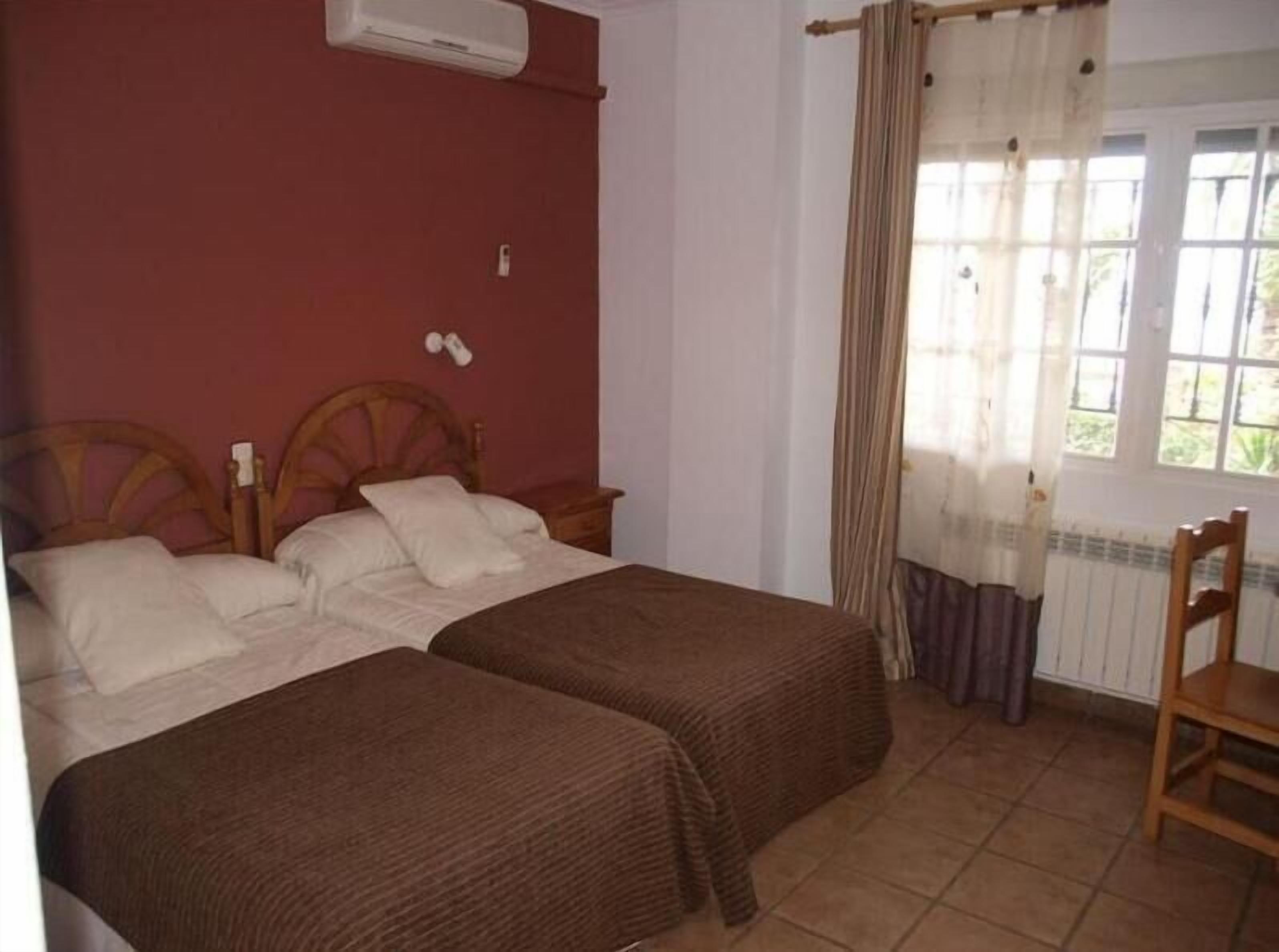 Un dormitorio con dos camas, cabecero de madera, una ventana con cortinas y un radiador.