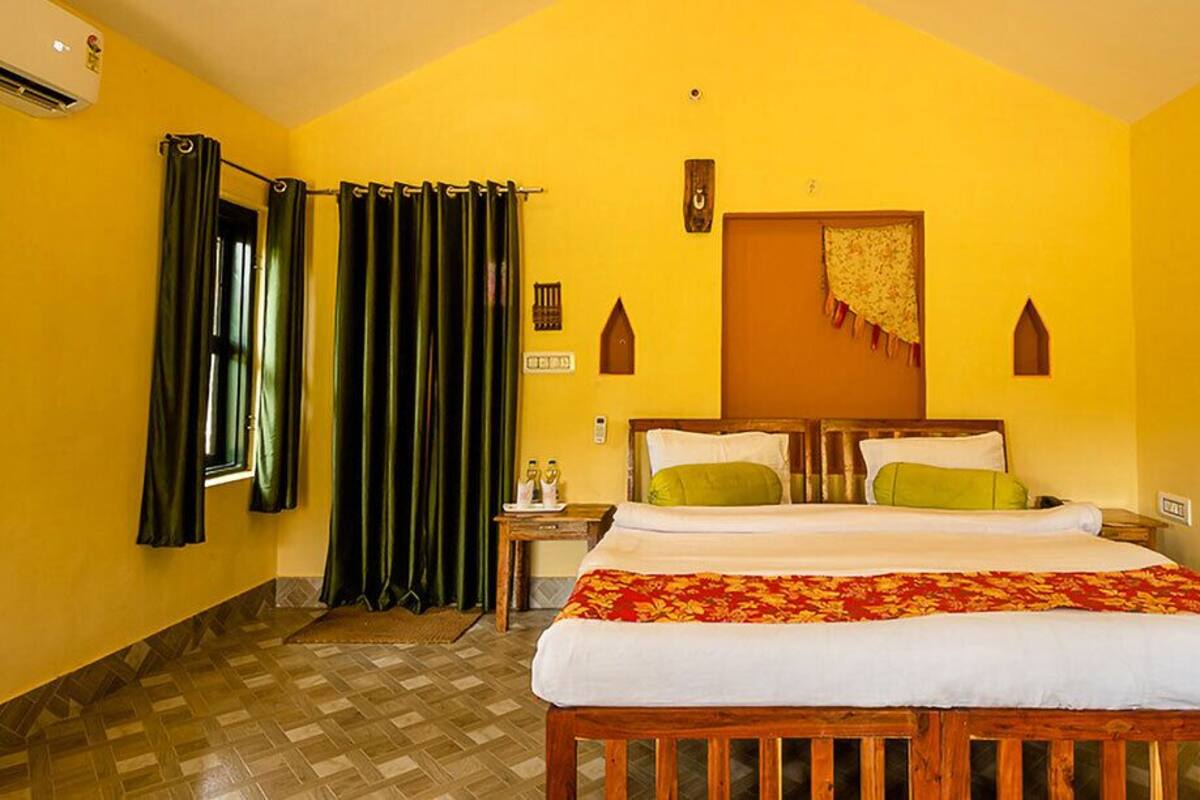 Quarto de hotel com uma cama grande, duas mesas de cabeceira, um painel de madeira na cabeceira, uma janela com cortinas e um ar condicionado fixado na parede.