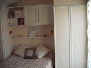 A bedroom with a bed, a wardrobe, and shelves with books and a framed picture.