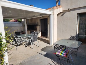 Een terras buiten met een tafel, stoelen, een barbecue en een overdekt gedeelte.