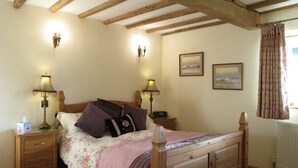 A bedroom with a wooden bed, two bedside tables with lamps, a radiator, and two framed pictures on the wall. - 5*Gold One bed near Ludlow, The Granary (Kidderminster)