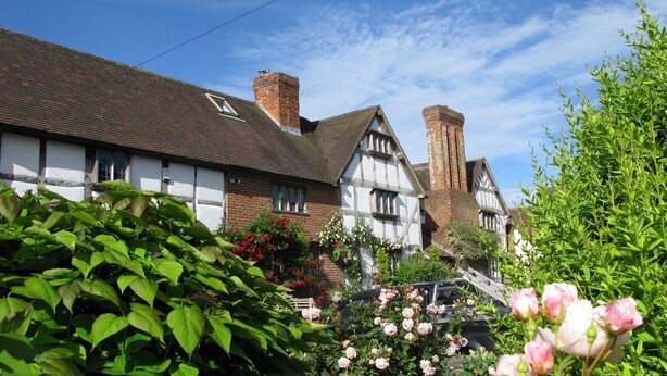 A traditional half-timbered house with a brick chimney, surrounded by lush greenery and flowering plants. - 5*Gold One bed near Ludlow, The Granary (Kidderminster)