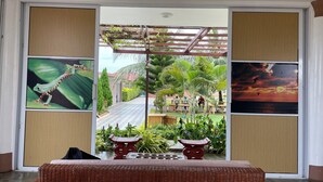 Una habitación con un amplio ventanal corredero que da a un espacio al aire libre con una pérgola, plantas y vistas a un atardecer sobre el agua.
