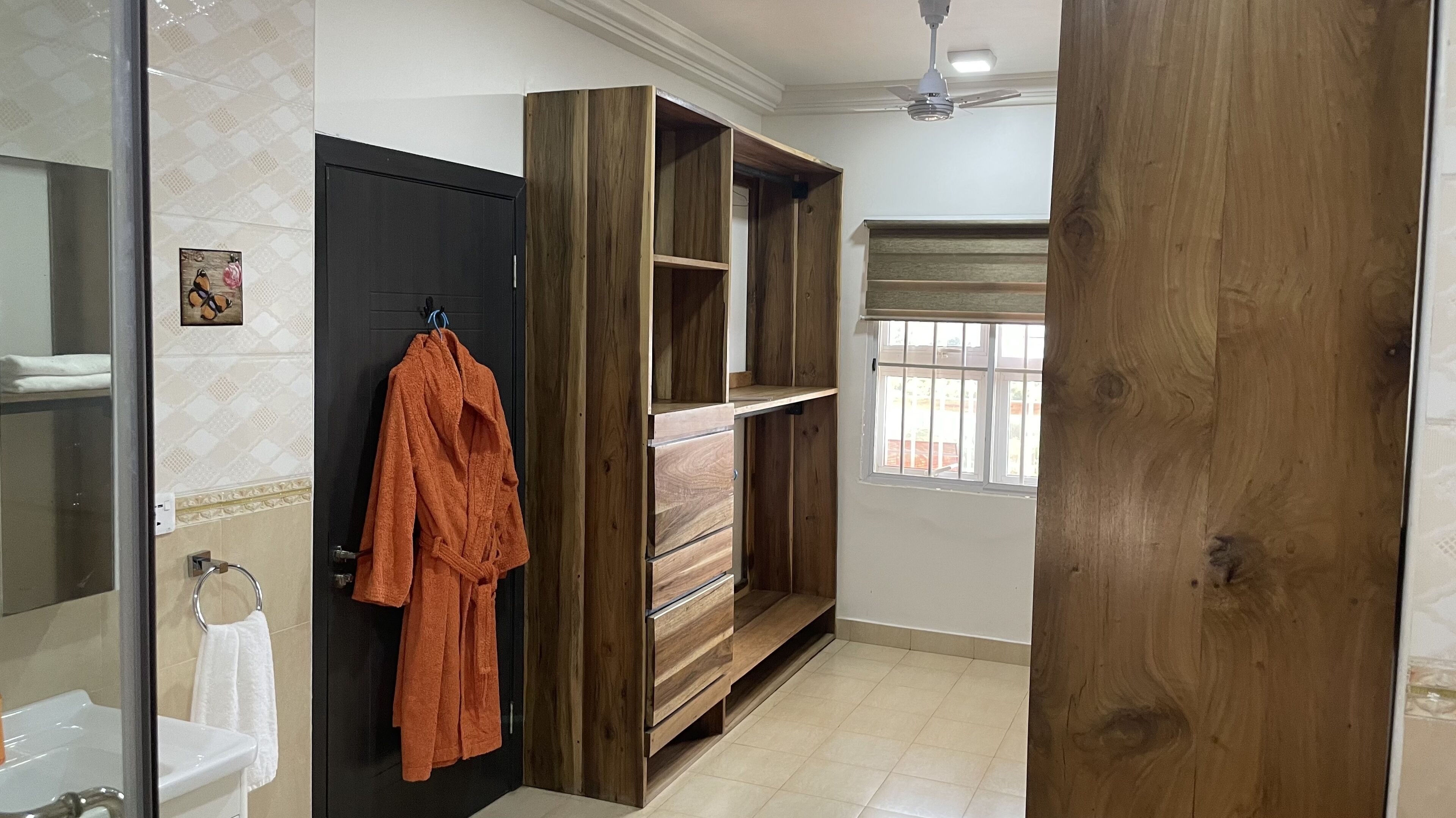 A bathroom with a wooden vanity, a towel rack with a robe, and a window with blinds.