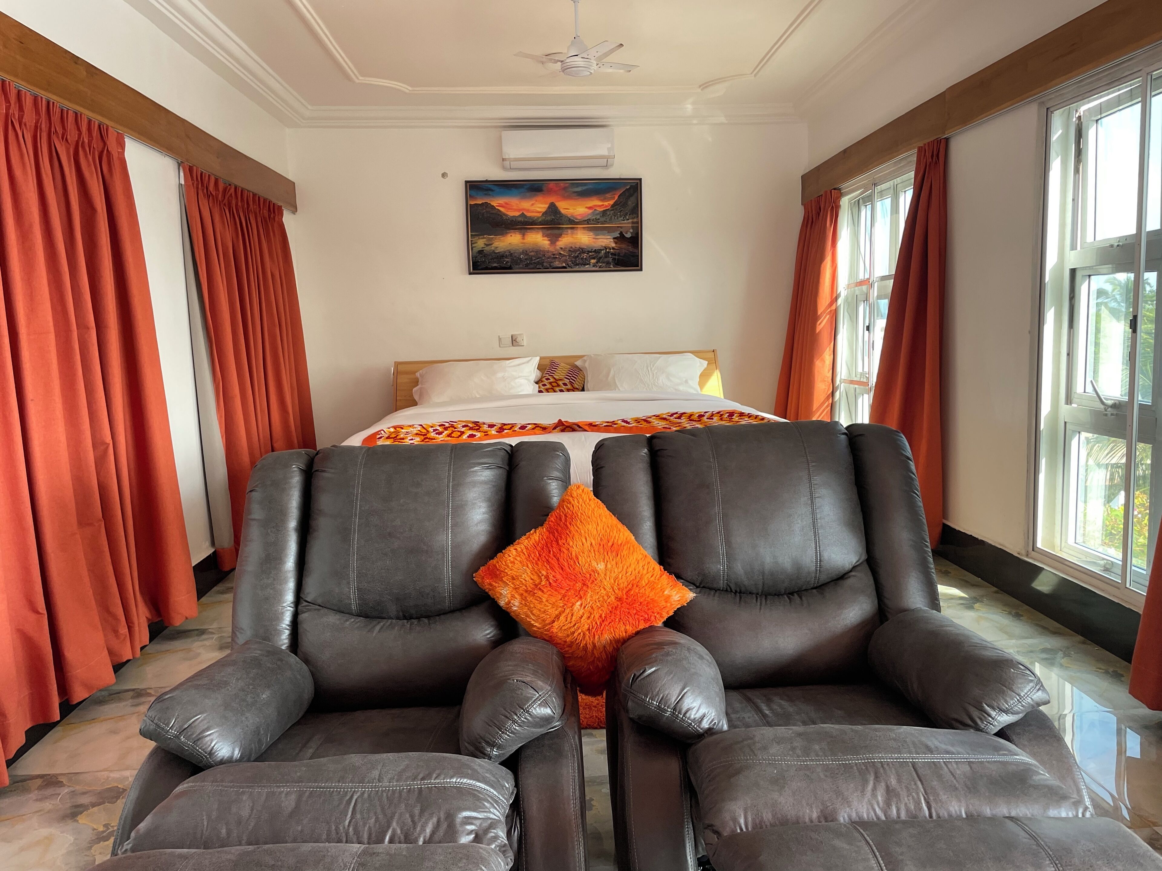 Una habitación de hotel con una cama, dos sillones de cuero, un ventanal grande y un cuadro en la pared.