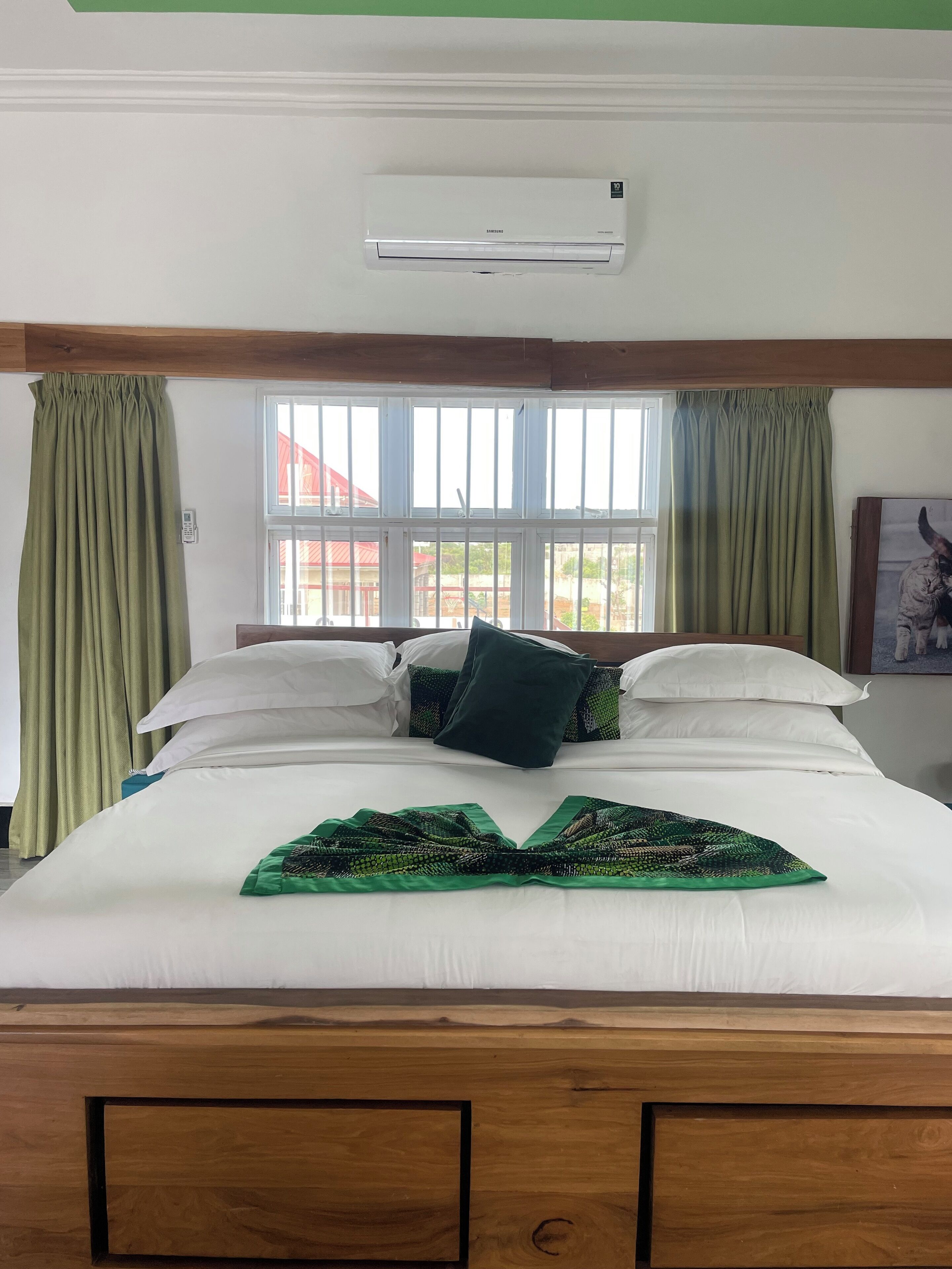 A neatly made bed with white and green bedding, a green throw, and a window with curtains.