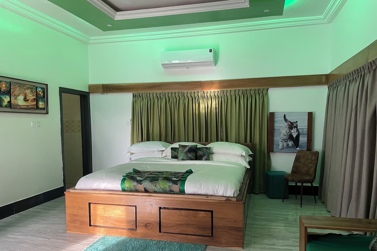 Quarto com cama, tapete verde, cabeceira de madeira, cadeira verde e um quadro na parede.