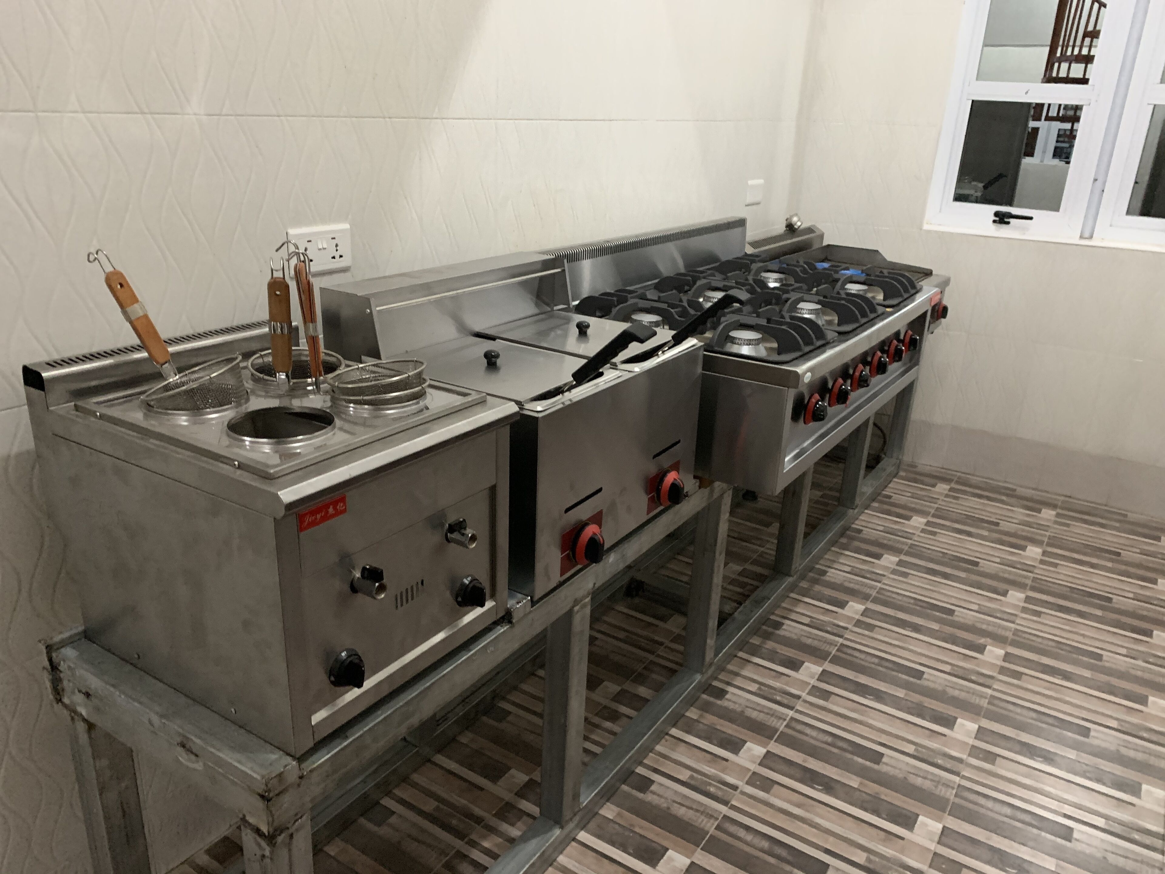 A commercial kitchen with stainless steel appliances, a tiled floor, and a window with a view of the outside.